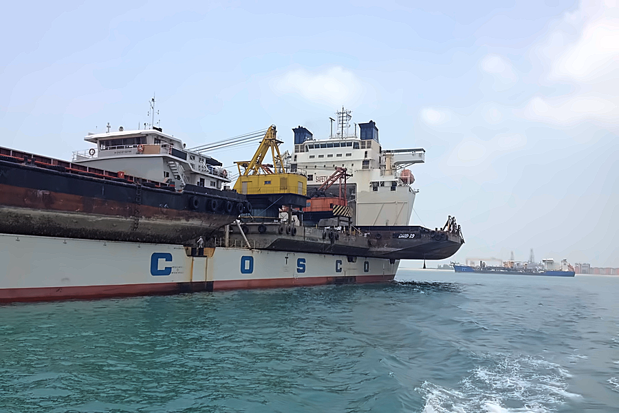 A heavy lift vessel working cargo alongside a barge at anchorage